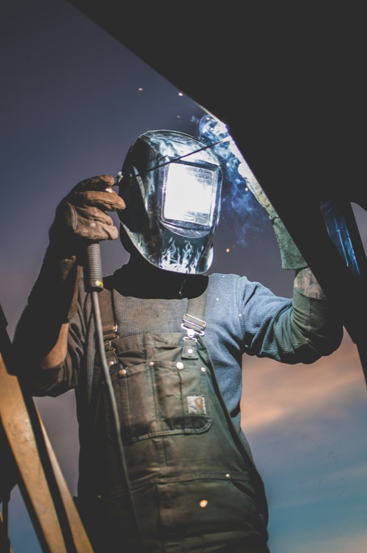 Welder in protective helmet working on structural steel.
