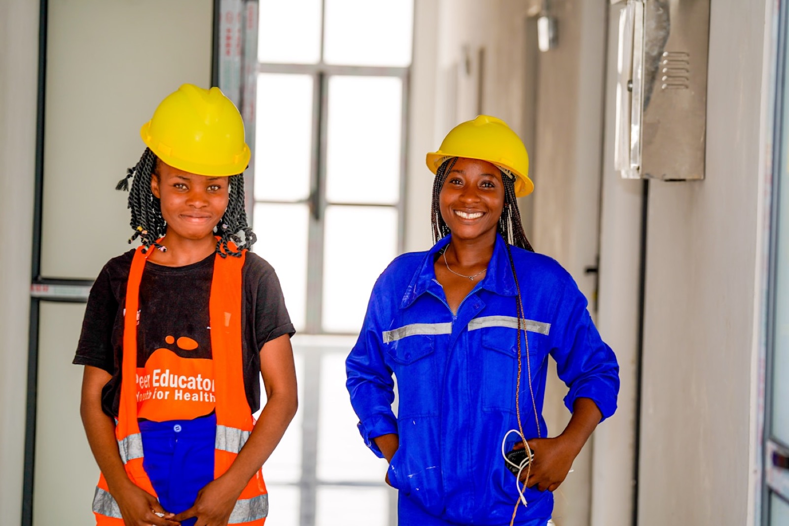 Two young Ugandan workers in hard hats inside a building under construction.