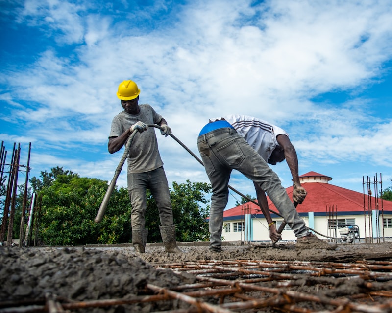 Workers spreading concrete over a steel reinforcement mat during a slab pour.