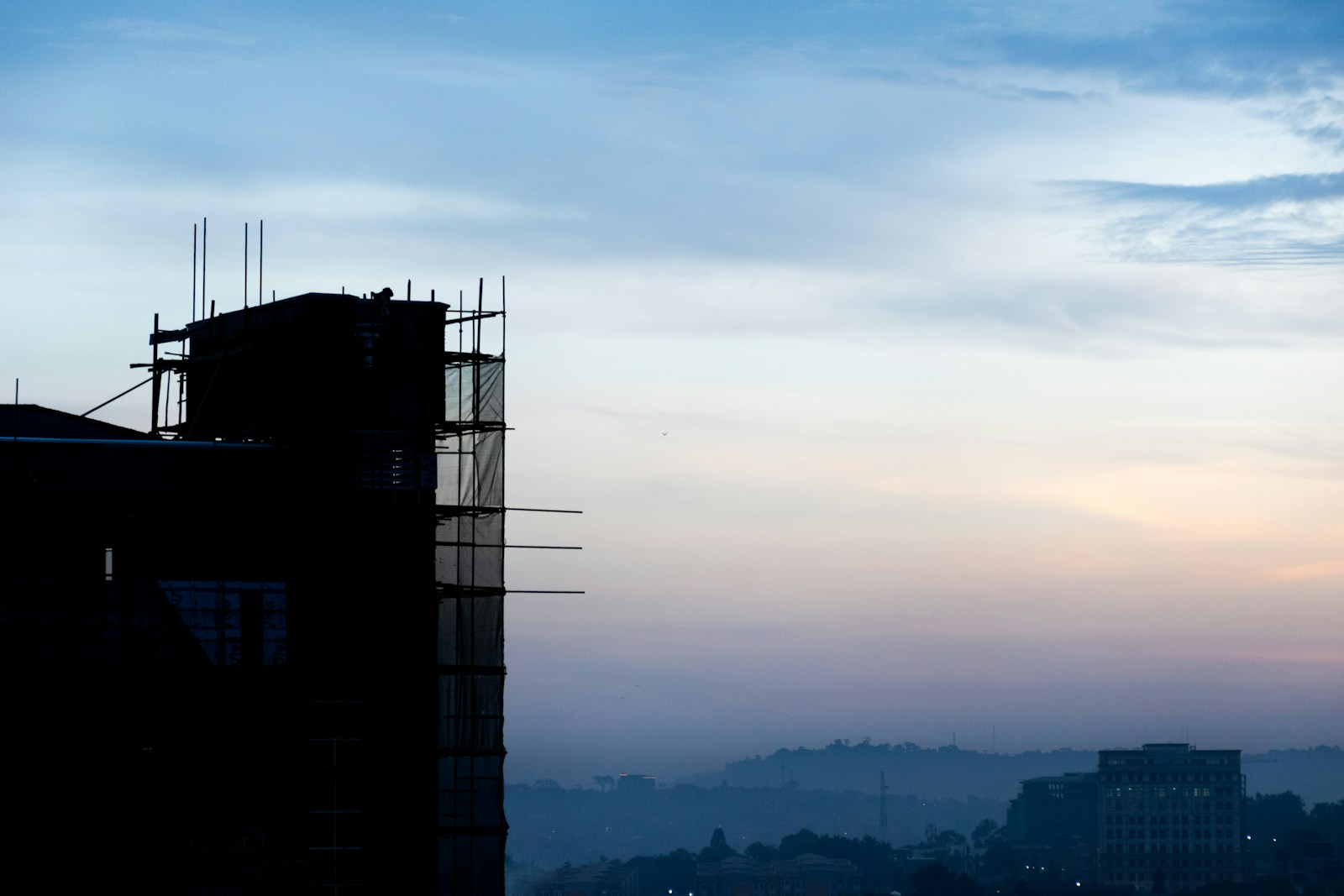 A building under construction silhouetted against the Kampala sunrise.